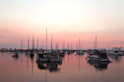 Sailboats moored in harbor at sunset