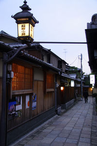 Illuminated street light by building against sky at dusk