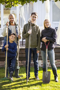 Portrait of confident family with gardening equipment standing at yard