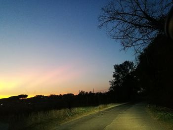 Road by silhouette trees against clear sky at sunset