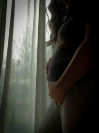 Side view of woman standing by window at home