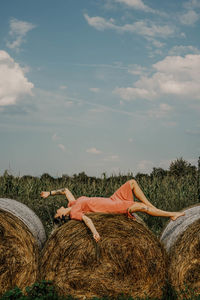 Full length of woman lying on hay bales against sky