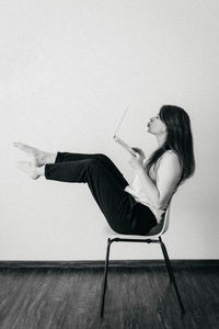 Side view of young woman sitting on chair against wall
