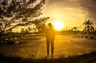 Silhouette man standing by palm trees during sunset