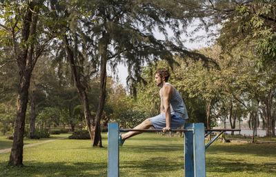 Side view of man exercising on metal rods at grassy field