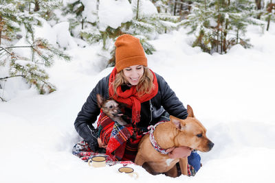 Portrait of woman with her two dogs wrapped in red checkered plaid on a snow in forest.