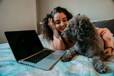 Smiling woman using laptop by dog on bed at home