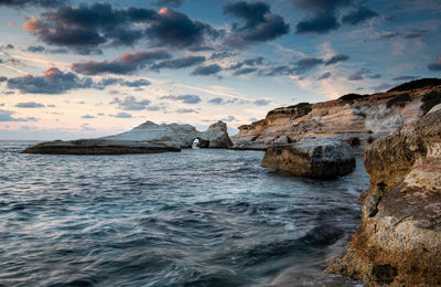 Rock formation in sea against sky during sunset