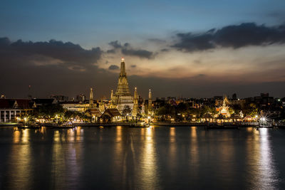 Illuminated buildings by river against sky at night