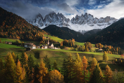 Spectacular view of rural houses on grass lawn near colorful trees and mounts under cloudy sky in fall