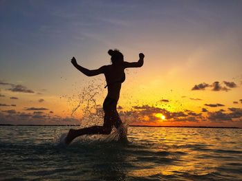 Woman running in sea against sky during sunset