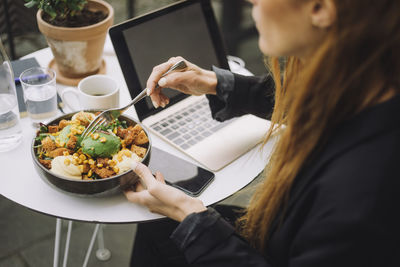 Businesswoman with bowl of meal and laptop at table