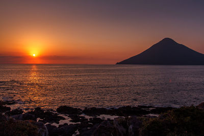 Scenic view of sea and silhouette mountain against sky during sunset