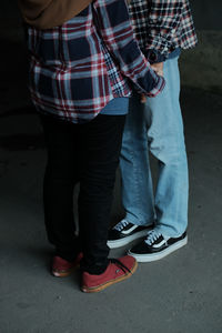 Low section of couple holding hands while standing against wall 