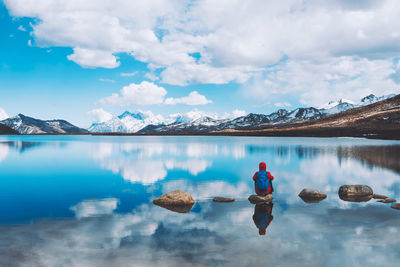 Hiker sitting on rock in lake against sky