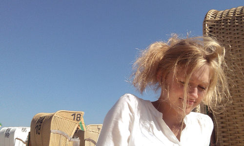 Low angle view of young woman against blue sky on sunny day