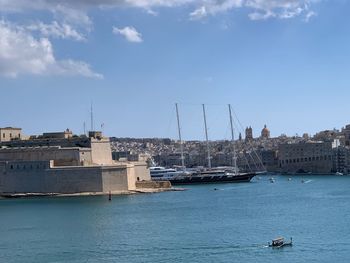 Sailboats in sea by buildings against sky