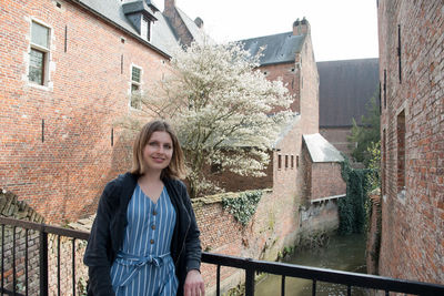 Smiling beautiful young girl stands on the old bridge under blossoming trees