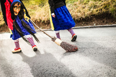 Rear view of people wearing witch costume with broom walking on street