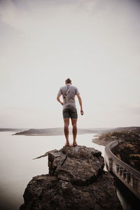 Rear view of man standing on cliff with sea in background against sky