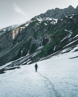 Rear view of man walking on snow covered land against sky