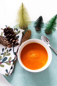 Flat lay view of carrot soup in bowl on pale green placemat surrounded with christmas decorations