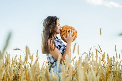 Teenager girl holding loaf of bread while standing amidst farm