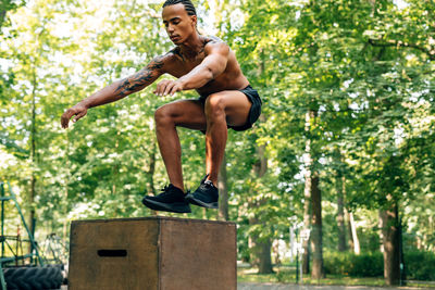 Shirtless male athlete jumping on box at park