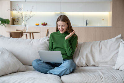 Glad woman looking at notebook screen, having video online conversation with friends, relatives