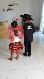 Rear view of siblings in halloween costumes standing at home