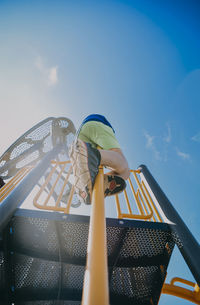 Low angle view of carefree boy climbing on metallic rod at playground against blue sky during sunny day