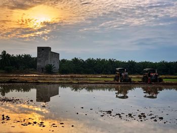 Reflection of building on field against sky during sunset