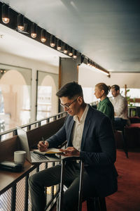 Businessman writing in diary while sitting with laptop at hotel