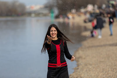 Mid-motion shot - smiling teen girl sitting on the shore of lake and throwing water in the air
