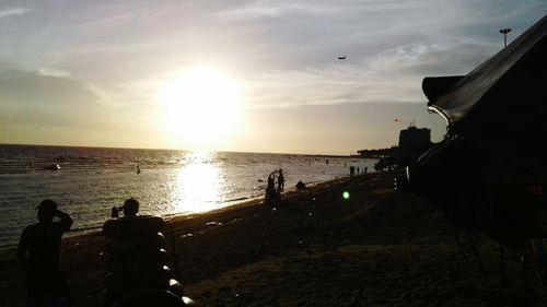 Silhouette people on beach against sky during sunset