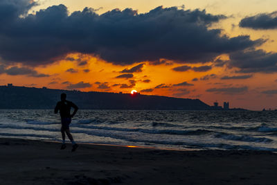 Silhouette man running at beach against sky during sunset