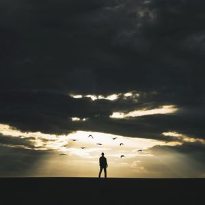 Silhouette of people on landscape against cloudy sky