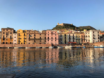 Buildings by river against clear blue sky