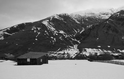 Houses on snow covered land by mountain against sky