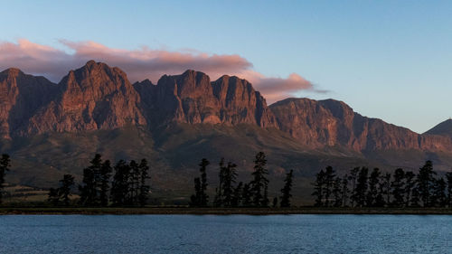 Scenic view of lake by mountains against sky during sunset