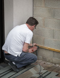 Man drilling wood on wall at home