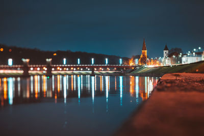 Illuminated buildings by river against sky at night