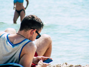 Rear view of man using mobile phone in sea