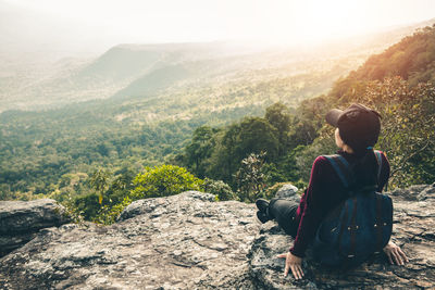 Rear view of man sitting on rock looking at mountains