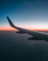 Airplane wing against sky during sunset