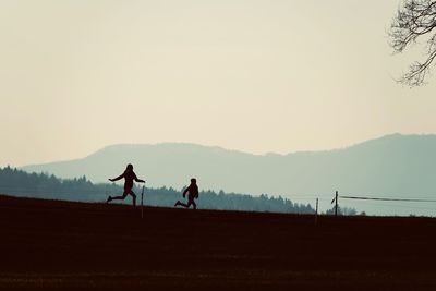 Silhouette people riding on mountain against clear sky