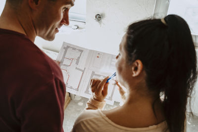 High angle view of couple discussing over blueprint while renovating home