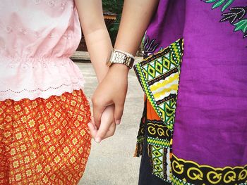 Midsection of friends holding hands on road