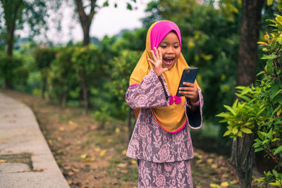 Full length of woman holding mobile phone while standing outdoors