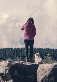Rear view of woman with dog standing on rock against sky
